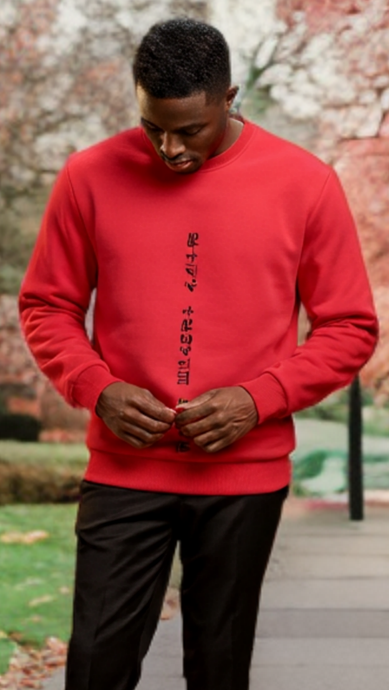 Person wearing a red sweatshirt with black text in a park with cherry blossom trees.