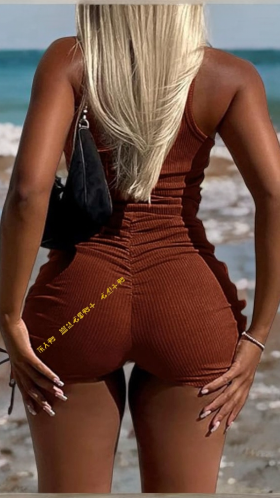Woman in a brown ribbed romper standing on a beach with ocean waves in the background