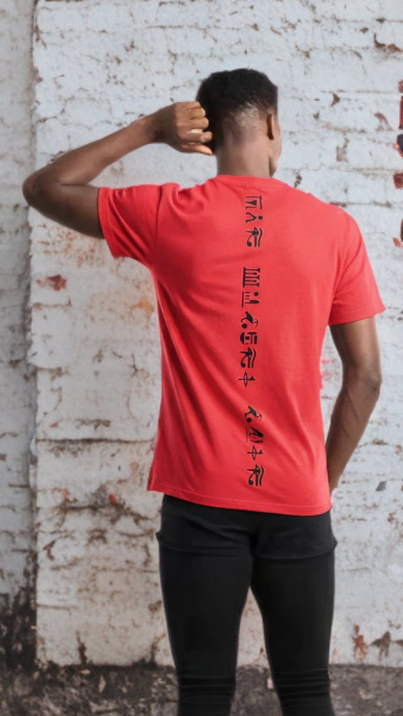 Person wearing a red t-shirt with black text standing against a textured white wall.