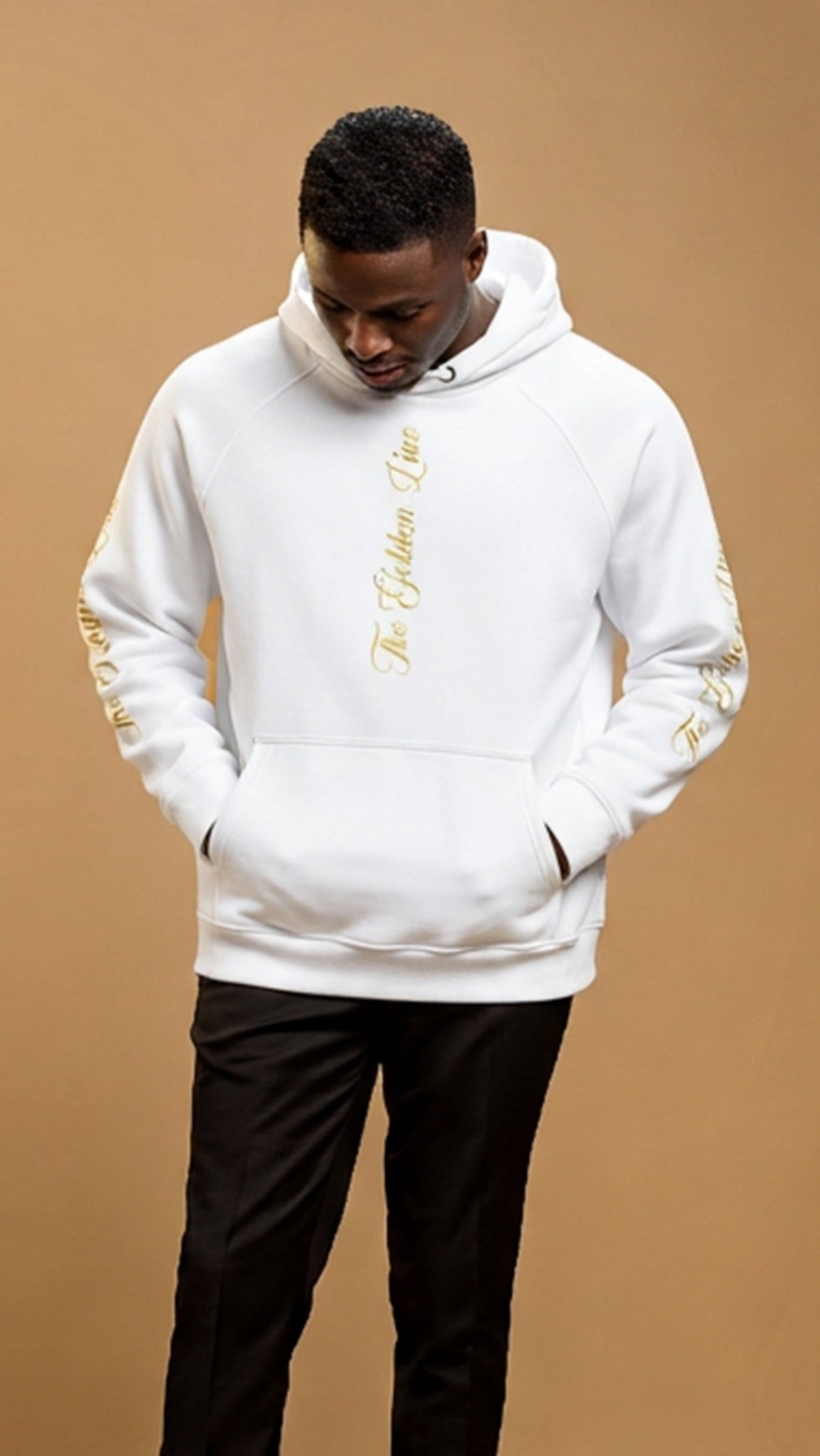 Person wearing a white hoodie with gold accents on a brown background