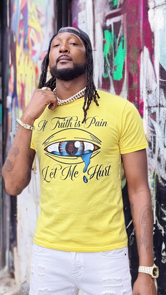 Man wearing a yellow t-shirt with graphic design and text, standing in front of a colorful mural.