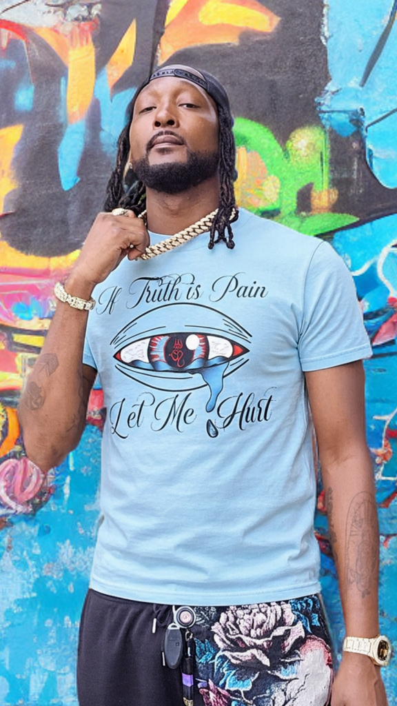 Person wearing a light blue t-shirt with graphic design and text, standing in front of a colorful graffiti wall.