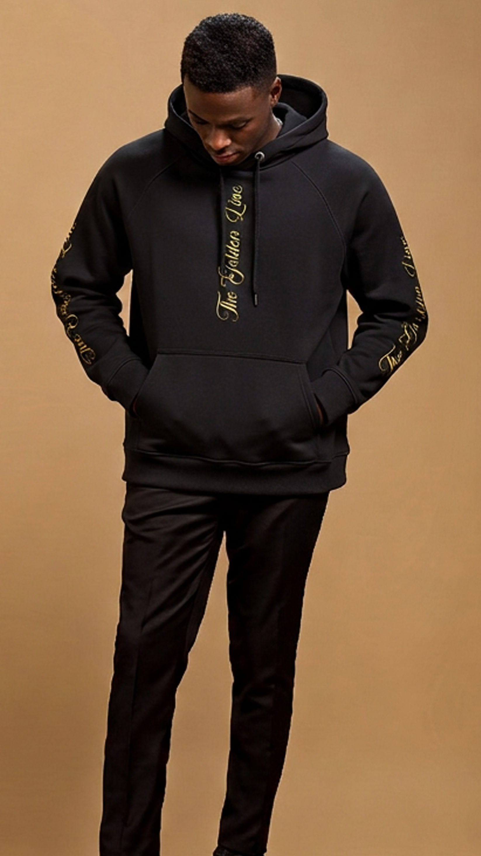 Man wearing a black hoodie and pants on a brown background