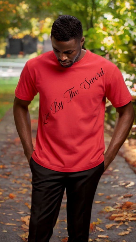 Man wearing a red t-shirt with text standing outdoors on a path with trees and grass.